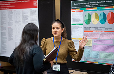 Image of a young woman speaking to another woman with a poster in the background.